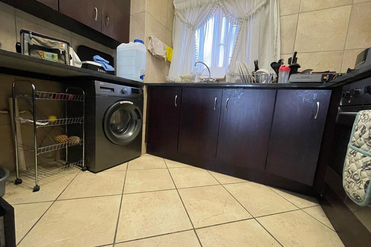 A functional kitchen featuring dark wood cabinetry, stone countertops, tiled flooring, and a built-in oven with integrated laundry plumbing.