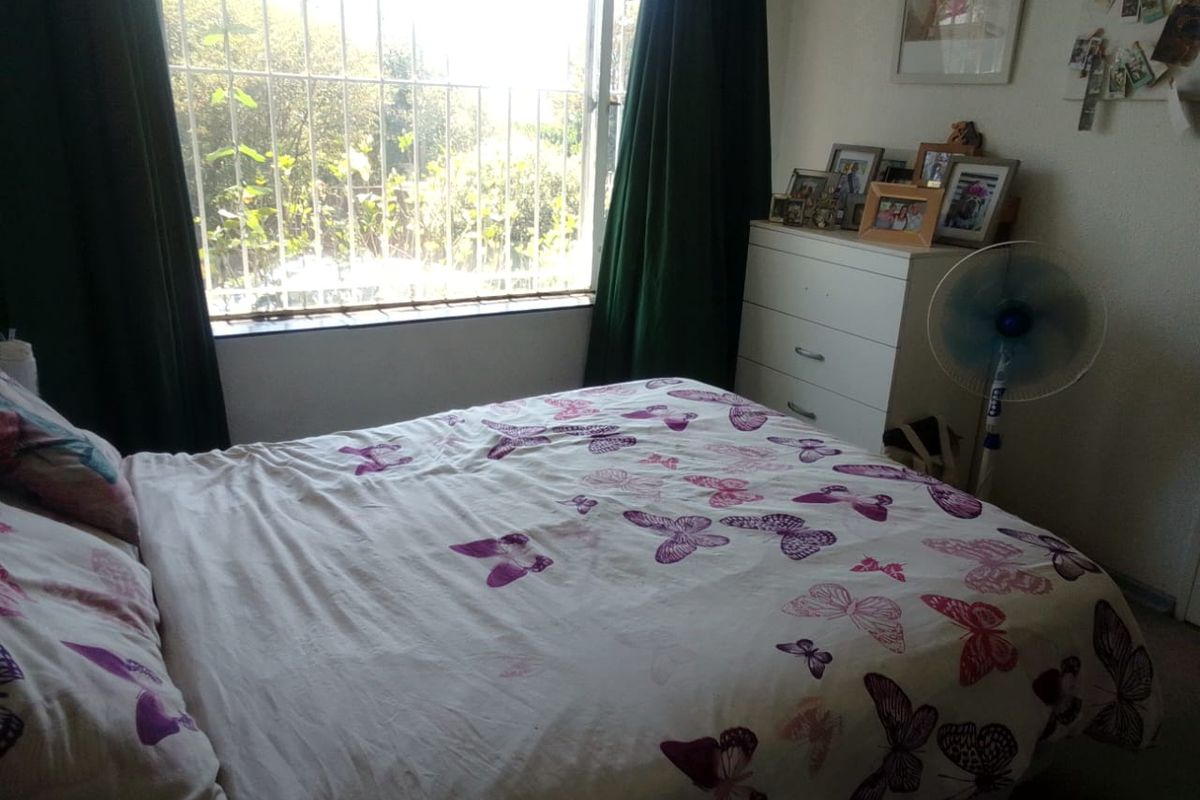 A standard bedroom featuring a window with security bars, providing natural light and a view of the exterior greenery.
