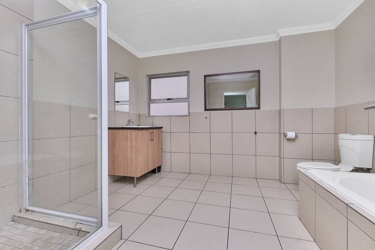 A spacious, neutral-toned bathroom featuring a separate shower enclosure, a built-in bathtub, a vanity basin, and a toilet with tiled finishes throughout.