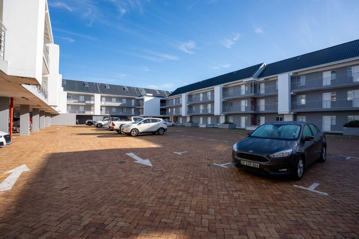 A view of the paved parking area and exterior facade of a modern multi-story apartment complex.