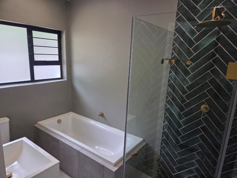 Modern bathroom featuring a built-in bathtub, a glass-enclosed shower with stylish herringbone tiling, and contemporary brass fixtures.