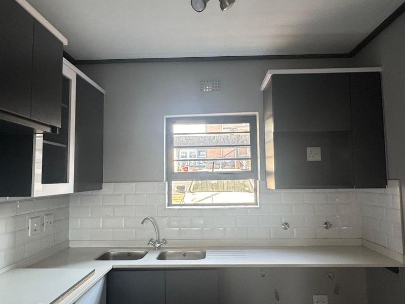 A modern kitchen featuring dark cabinetry, a double sink, and a white subway tile backsplash, currently awaiting appliance installation.