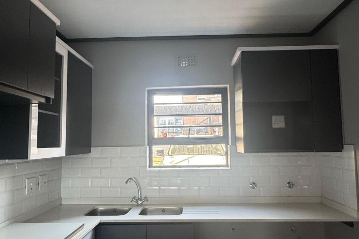 A modern kitchen featuring dark cabinetry, a double sink, and a white subway tile backsplash, currently awaiting appliance installation.