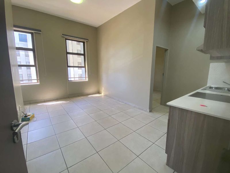 An open-plan living and kitchen area featuring neutral tiled flooring, built-in cabinetry, and large windows providing ample natural light.