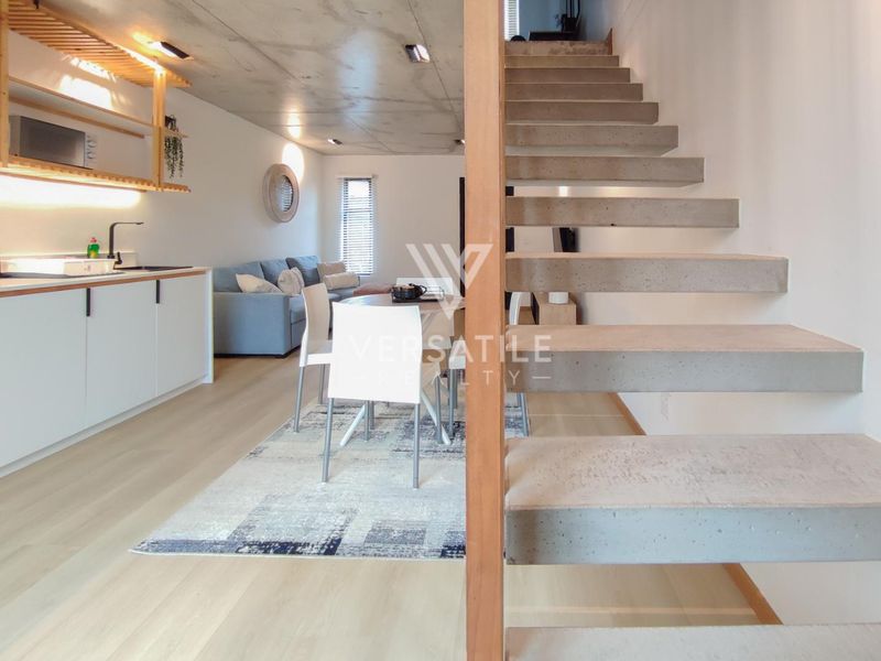 Modern open-plan living area featuring a sleek kitchen, exposed concrete ceiling, and a striking floating concrete staircase.
