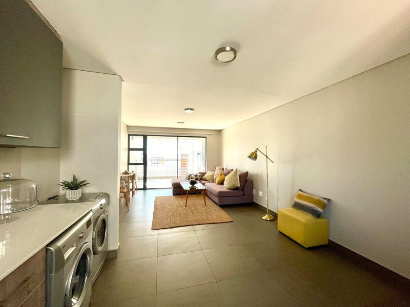Modern open-plan living area featuring tiled floors, sleek kitchen cabinetry with stone countertops, and a sliding door leading to a private balcony.