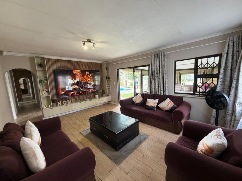 Spacious living room featuring a modern built-in media wall, tiled flooring, and large sliding doors providing direct access to the outdoor patio and pool area.
