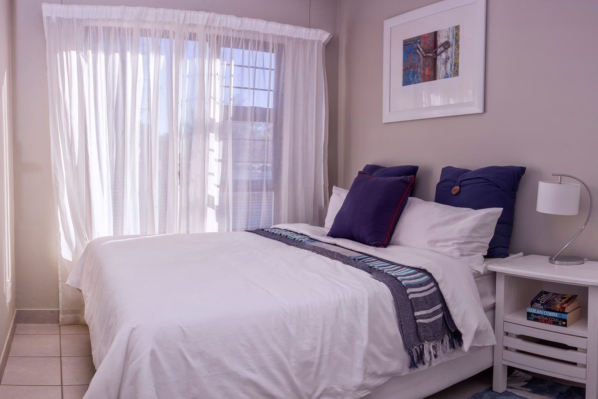A well-lit bedroom featuring neutral wall tones, tiled flooring, and a large window with sheer curtains, providing a bright and comfortable living space.