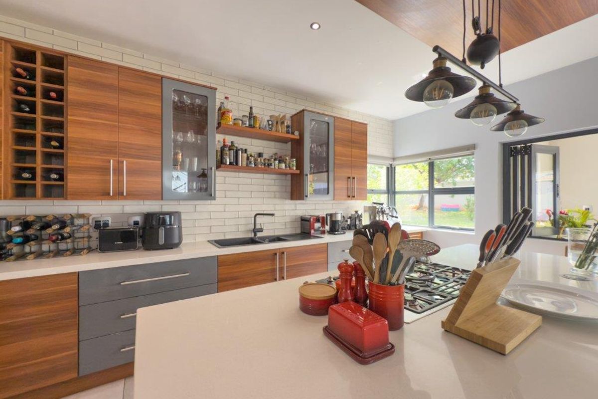 Modern kitchen featuring wood-grain cabinetry, stone countertops, a central island with a built-in gas hob, and subway tile backsplash.