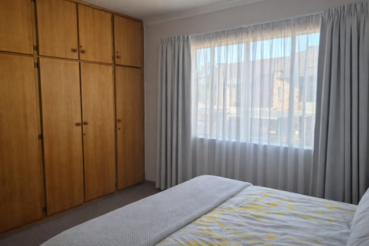 A bedroom featuring floor-to-ceiling built-in wooden cabinetry and large windows with curtains, providing ample storage and natural light.
