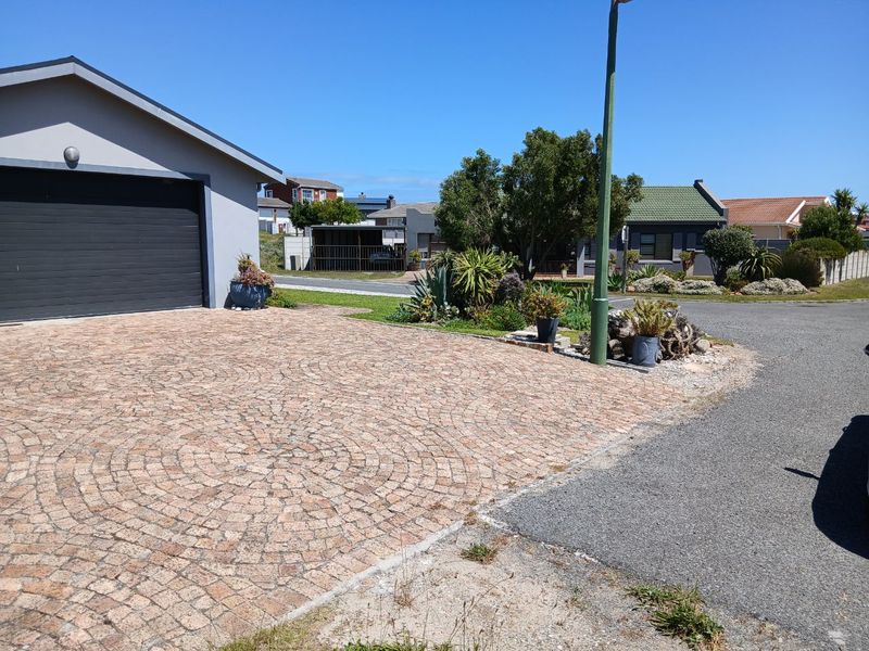 A well-maintained residential front exterior featuring a decorative cobblestone driveway, a single garage, and established garden landscaping.