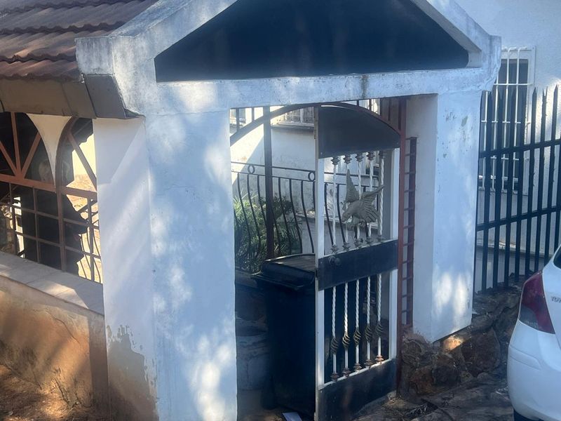 Front entrance gate with masonry pillars and metal security fencing, showing signs of weathered exterior paint.