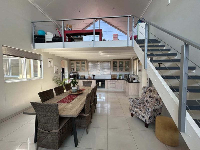 Spacious open-plan living and kitchen area featuring a mezzanine level, vaulted ceilings, modern tiled flooring, and a contemporary staircase with stainless steel railings.