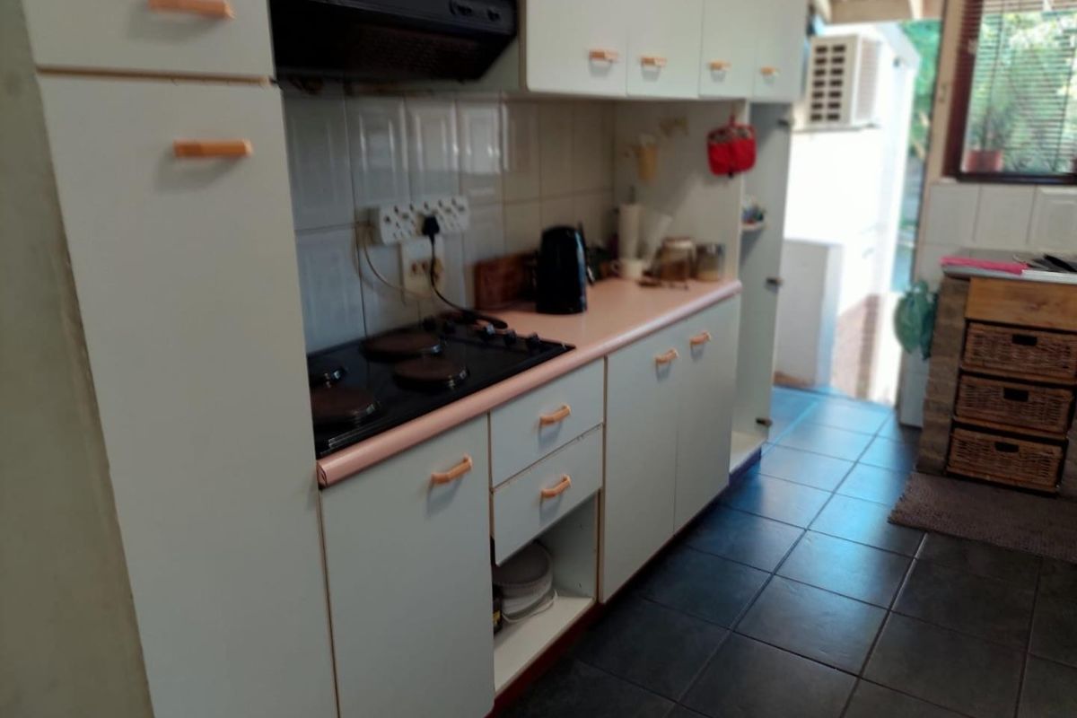 A functional kitchen featuring built-in cabinetry, an electric hob with an extractor fan, tiled splashbacks, and dark floor tiles.