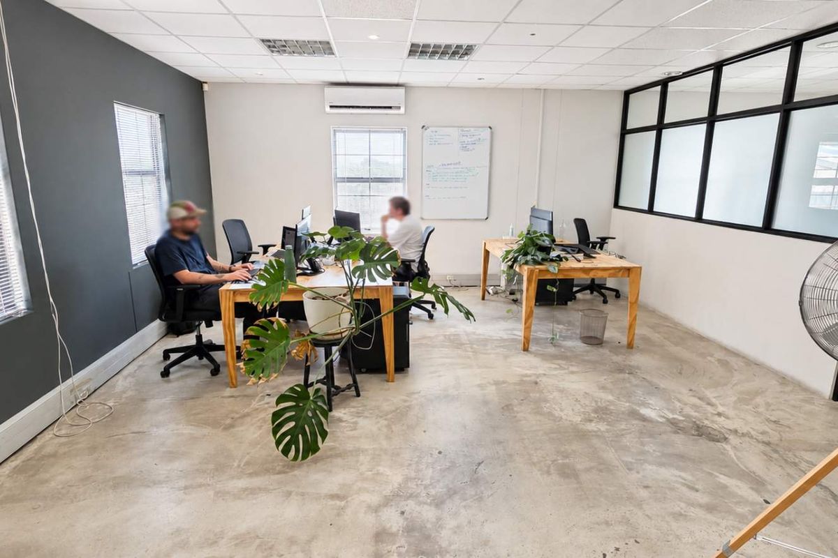 A modern open-plan office space featuring polished concrete floors, a suspended ceiling, and a black-framed glass partition wall.