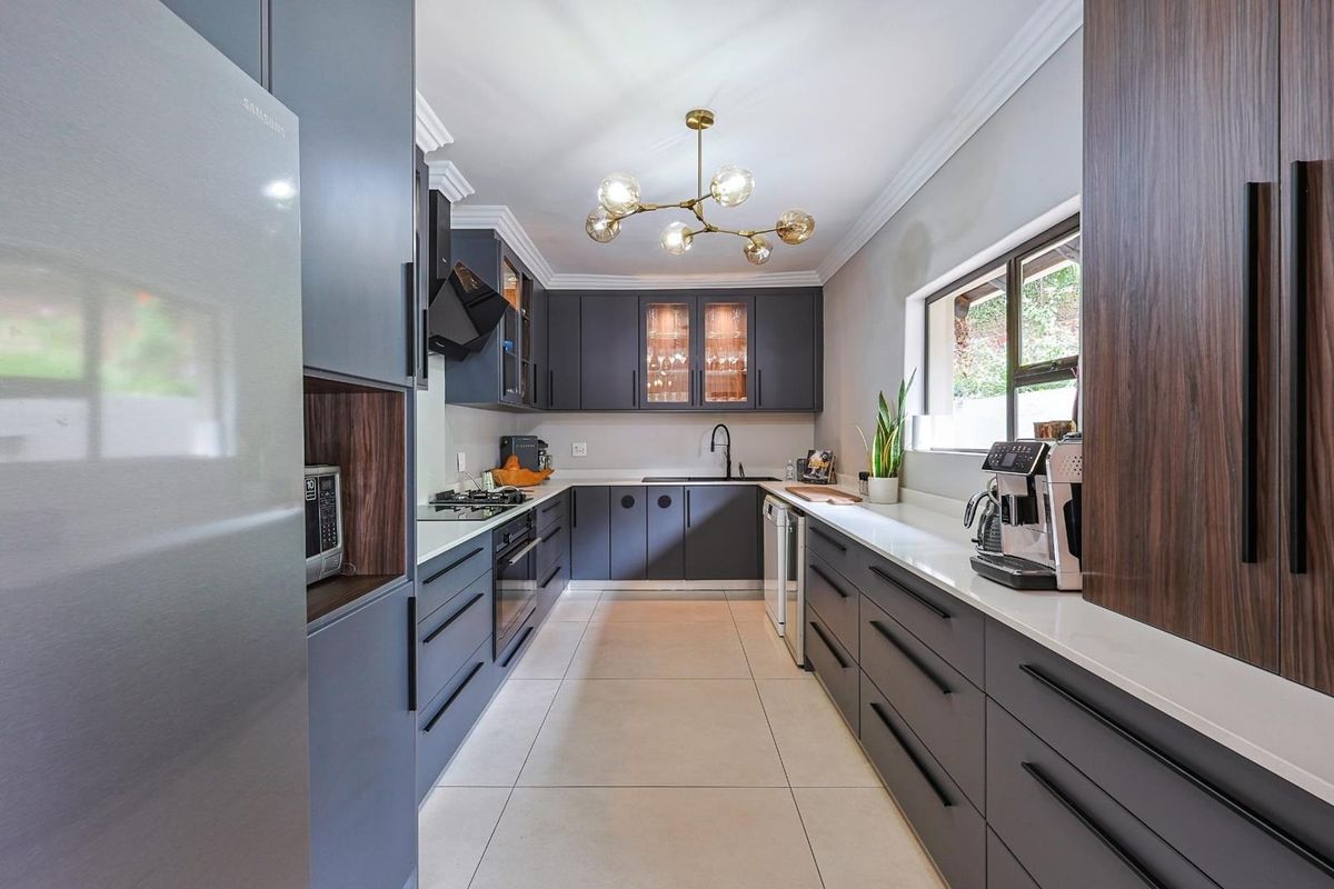 Modern galley-style kitchen featuring dark cabinetry, stone countertops, integrated oven, gas hob, and contemporary pendant lighting.
