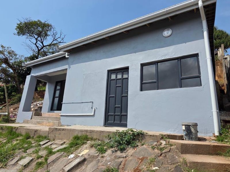 Exterior view of the rear of the property featuring grey painted walls, dark aluminium window frames, and concrete steps leading to the entrance.