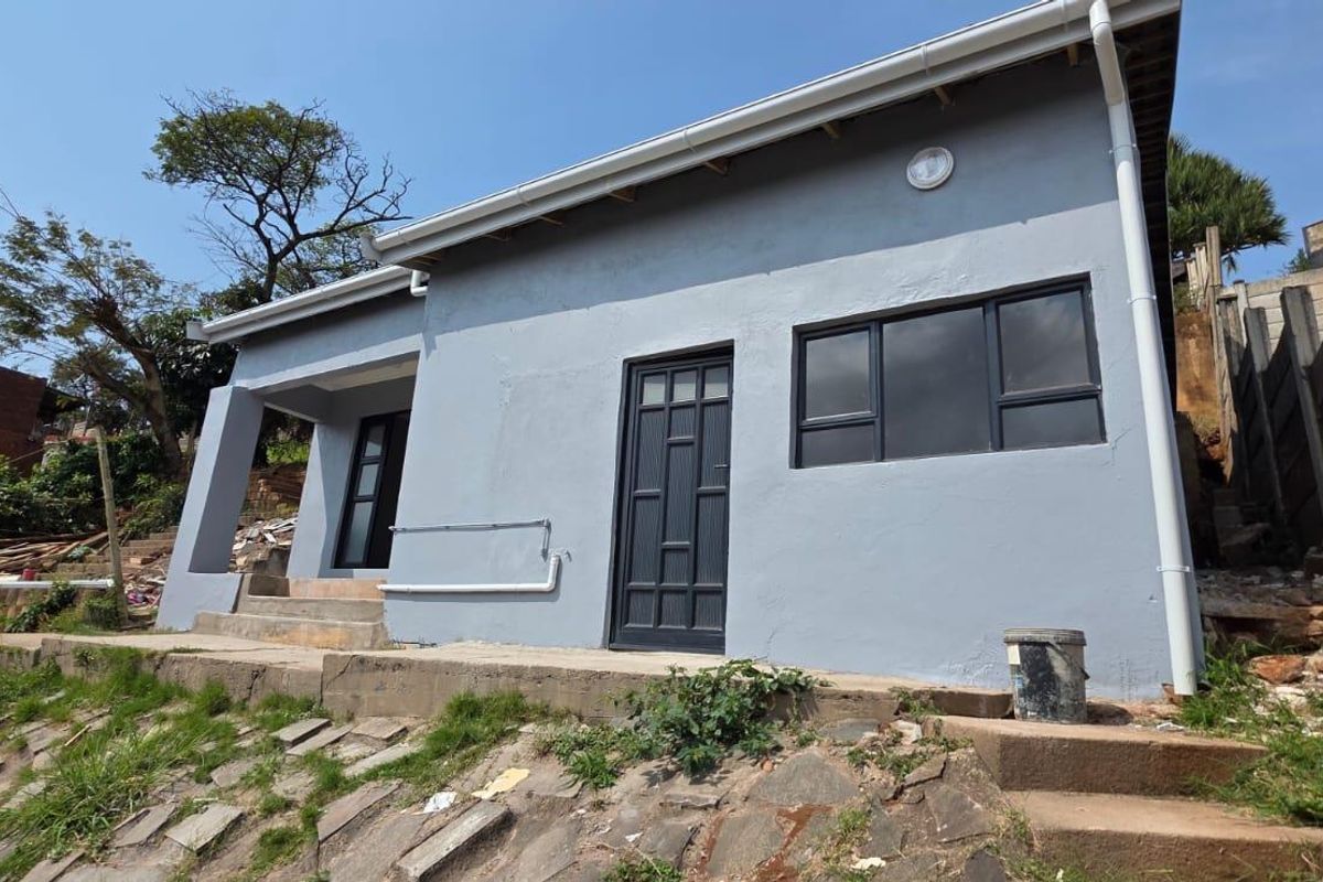 Exterior view of the rear of the property featuring grey painted walls, dark aluminium window frames, and concrete steps leading to the entrance.