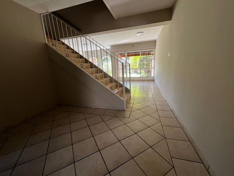 An empty, open-plan living area featuring tiled flooring, a staircase with a metal balustrade, and a sliding glass door leading to the exterior.