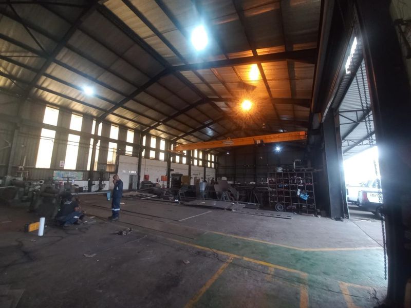 Spacious industrial warehouse featuring a high-clearance steel portal frame, overhead gantry crane, and large roller shutter access, suitable for manufacturing or storage operations.