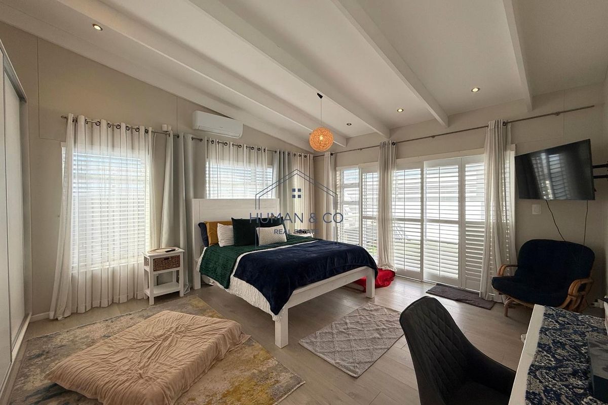 Spacious bedroom featuring high vaulted ceilings with exposed beams, recessed lighting, air conditioning unit, and large glass sliding doors leading to the exterior.