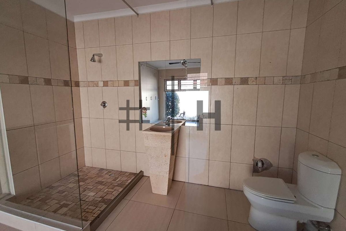 A functional bathroom featuring a walk-in shower with glass enclosure, a pedestal basin, and a standard toilet with neutral wall and floor tiling.