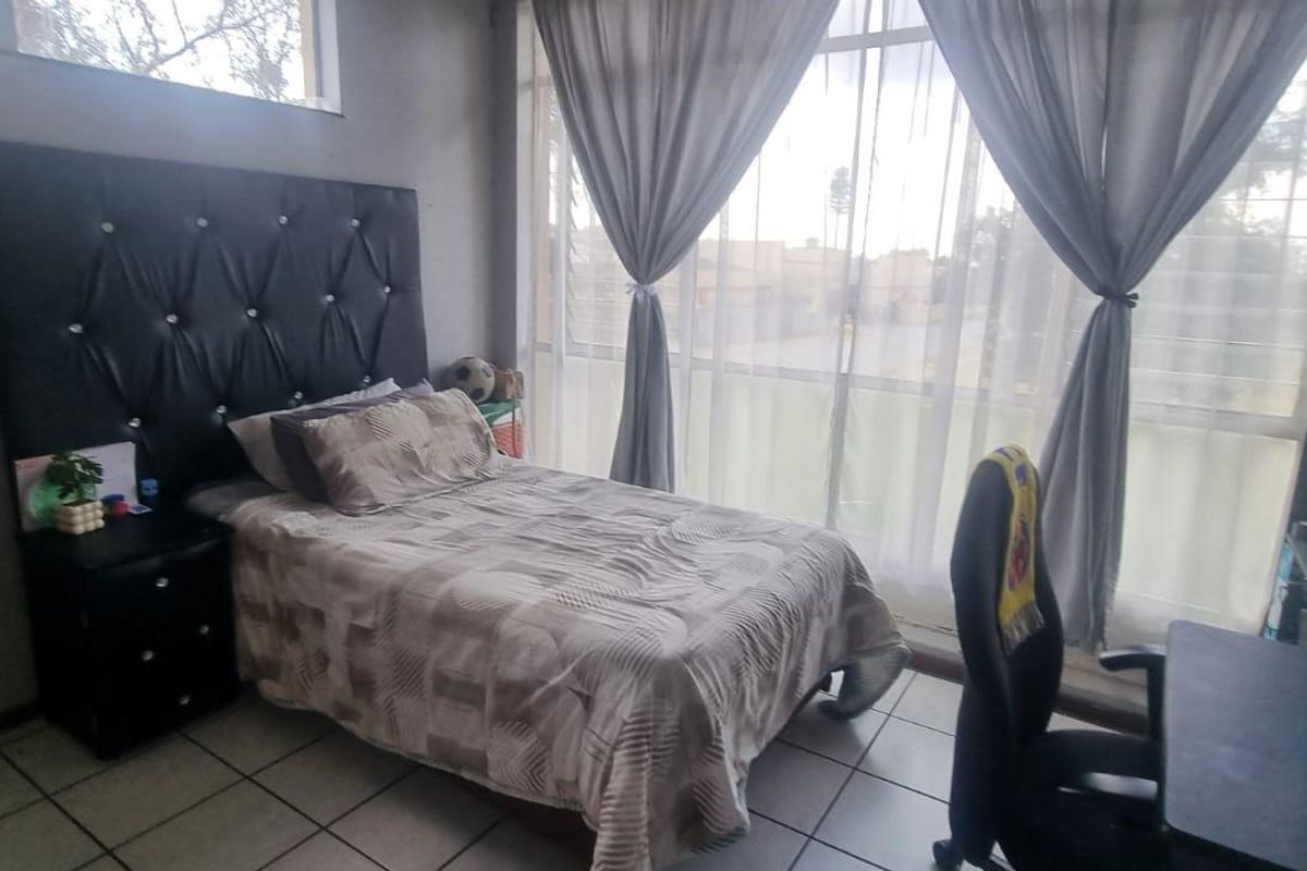 A bedroom featuring large windows with natural light, tiled flooring, and a neutral wall finish.