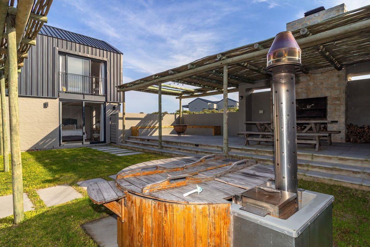 Spacious rear garden featuring a wood-fired hot tub, a covered patio with a built-in braai, and modern architectural finishes.