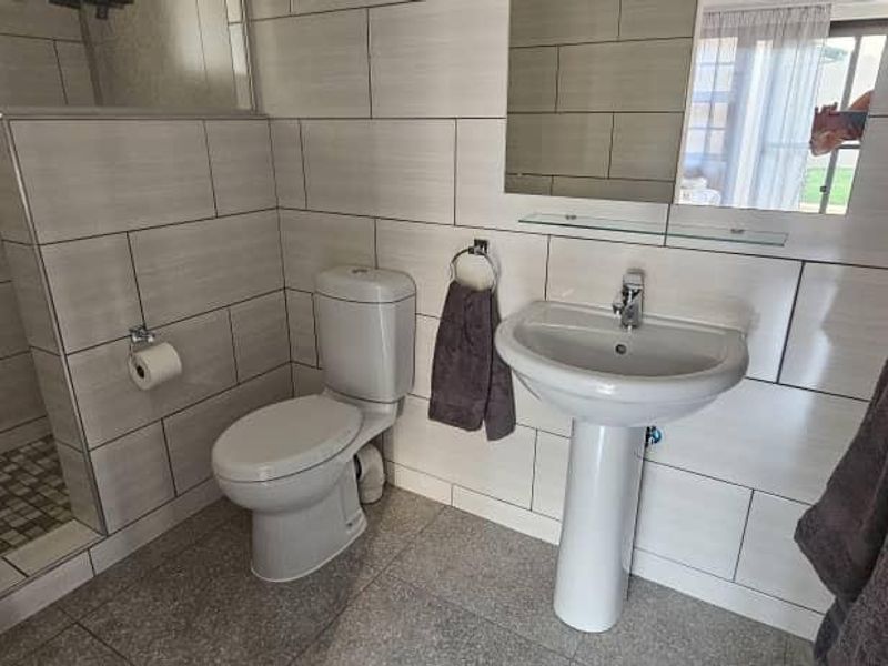 A modern, well-maintained bathroom featuring a pedestal basin, toilet, and a walk-in shower with neutral wall and floor tiling.