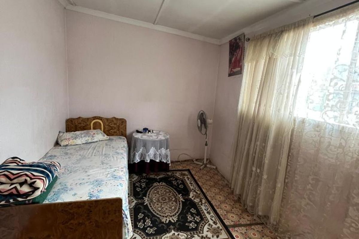 A bedroom featuring patterned floor tiles and a simple ceiling finish, offering a functional space with natural light from the window.