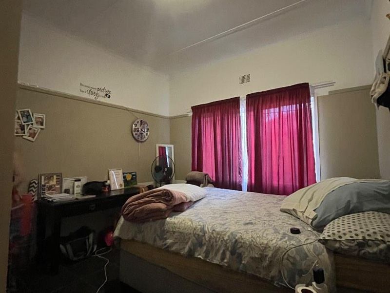 A bedroom featuring a picture rail and ventilation grille, with neutral wall tones and dark flooring.