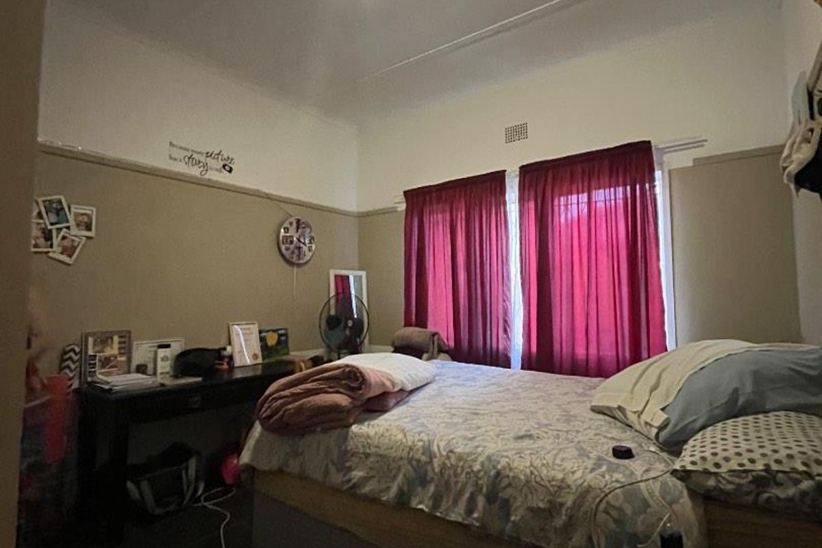 A bedroom featuring a picture rail and ventilation grille, with neutral wall tones and dark flooring.