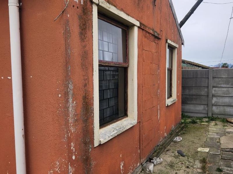 Rear exterior view of the property showing weathered orange painted walls, window frames, and paved ground area requiring maintenance.
