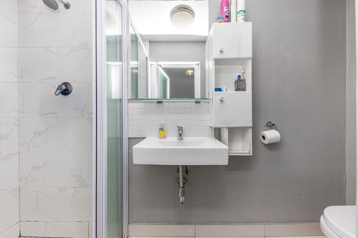 A compact bathroom featuring a wall-mounted basin, integrated storage cabinet, and a glass-enclosed shower with marble-look wall tiles.