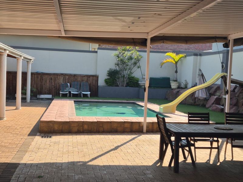 Outdoor entertainment area featuring a covered patio, paved flooring, and a swimming pool with a slide, set within a walled garden.