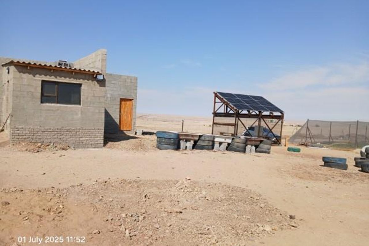Rear view of a small holding property featuring an unfinished masonry structure and a ground-mounted solar panel array in a rural setting.