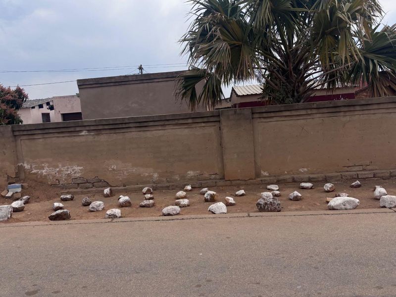 Street view showing a weathered boundary wall and pavement area with decorative stones.