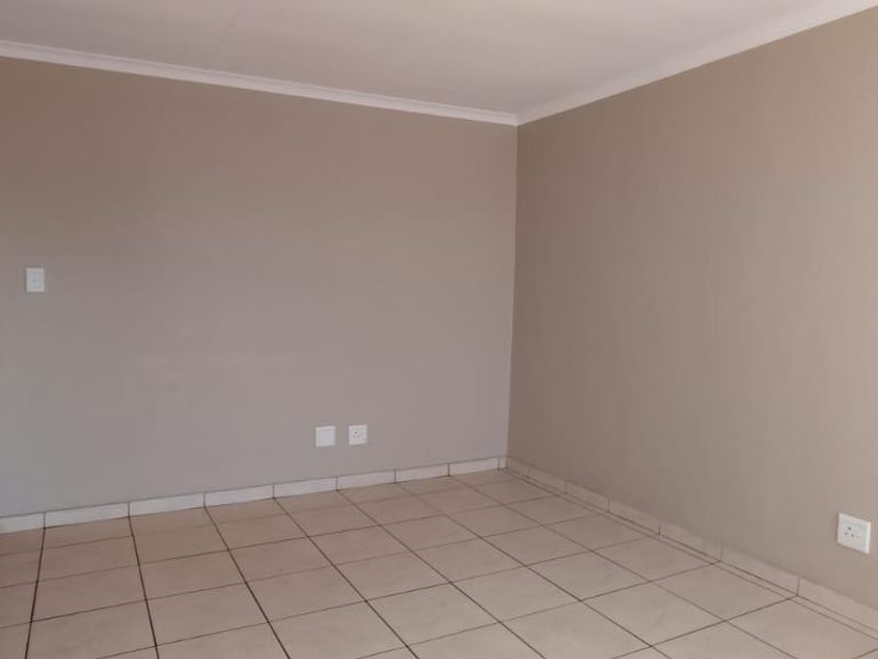 An empty living room featuring neutral painted walls, tiled flooring, and a solid wooden door.