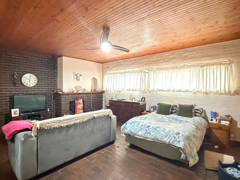 Spacious bedroom featuring a timber-clad ceiling, exposed brick fireplace, and tiled flooring, offering a rustic aesthetic with potential for modern updates.
