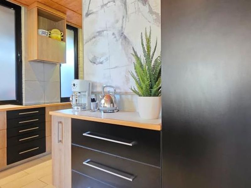 Modern kitchen featuring a mix of light wood and black cabinetry, sleek countertops, and large windows providing ample natural light.