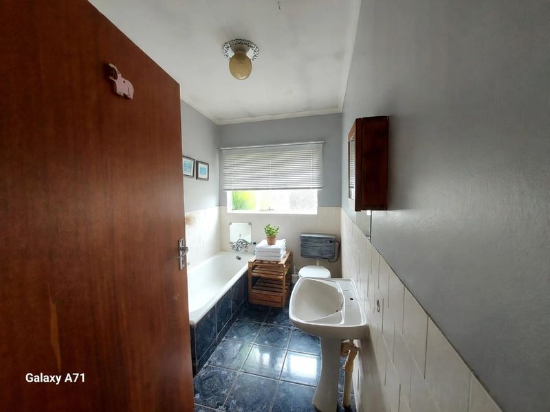 A functional bathroom featuring a bathtub, pedestal sink, and toilet with tiled flooring and wall splashbacks.