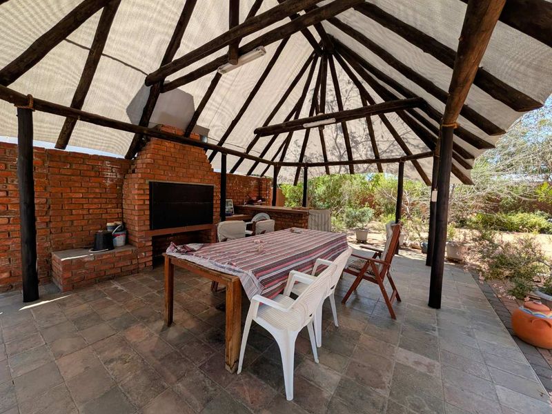 Covered outdoor patio area featuring a built-in brick braai, tiled flooring, and a rustic thatched roof structure, ideal for outdoor entertaining.