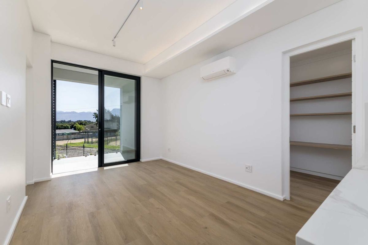 A bright, modern living area featuring laminate flooring, a split-system air conditioner, and a sliding glass door leading to an outdoor space.