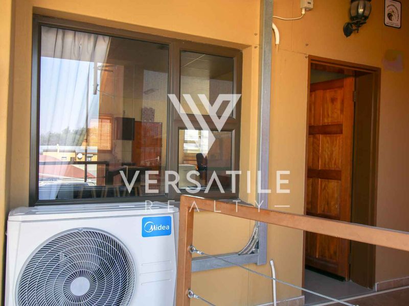 A covered balcony area featuring an external air conditioning unit, a wooden door, and an aluminium-framed window.
