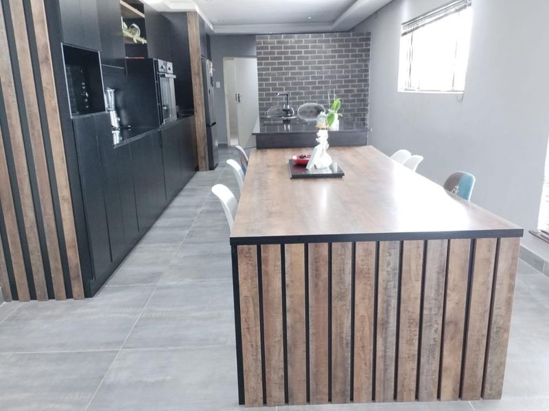Modern open-plan kitchen featuring dark cabinetry, a large timber-look island, and an exposed brick feature wall with high-quality tiled flooring.