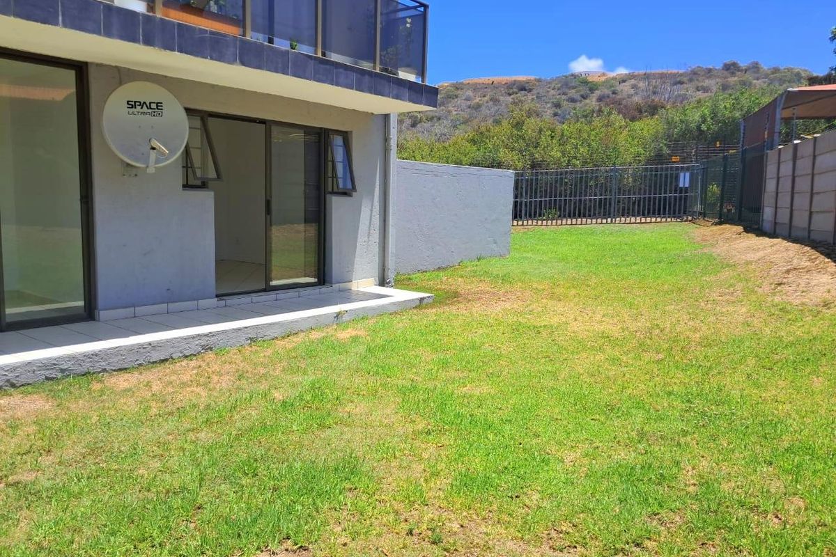 Rear view of the apartment featuring a private garden, tiled patio area, and sliding glass doors leading into the living space.