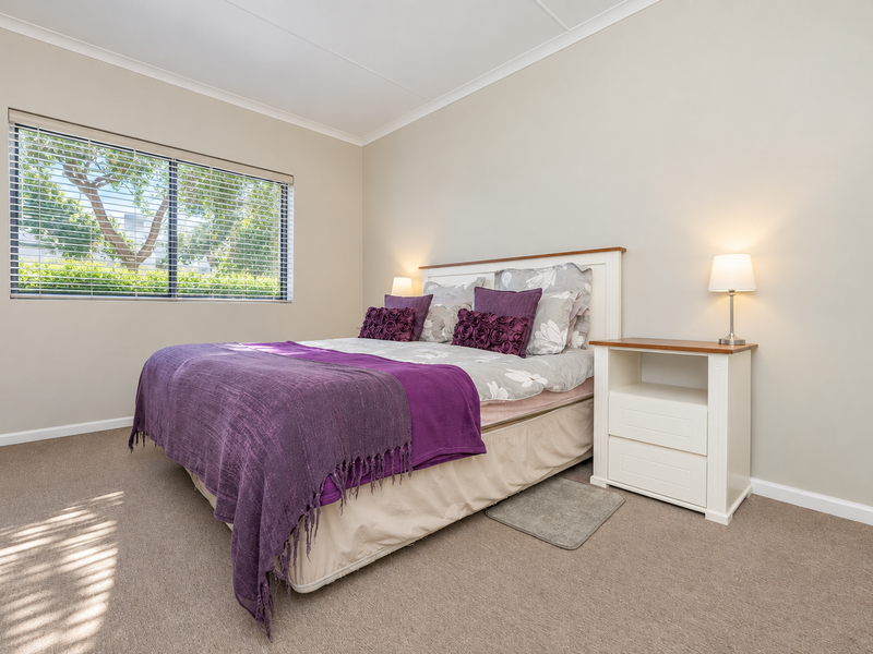 A well-maintained bedroom featuring neutral wall tones, carpeted flooring, and a window fitted with venetian blinds, providing a bright and comfortable living space.