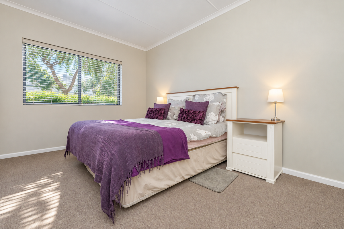 A well-maintained bedroom featuring neutral wall tones, carpeted flooring, and a window fitted with venetian blinds, providing a bright and comfortable living space.