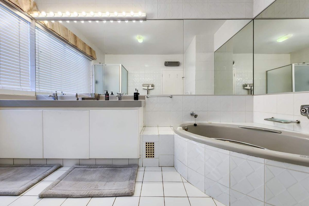 A spacious bathroom featuring a built-in vanity, large wall mirror, and a tiled bathtub area with a separate shower enclosure.