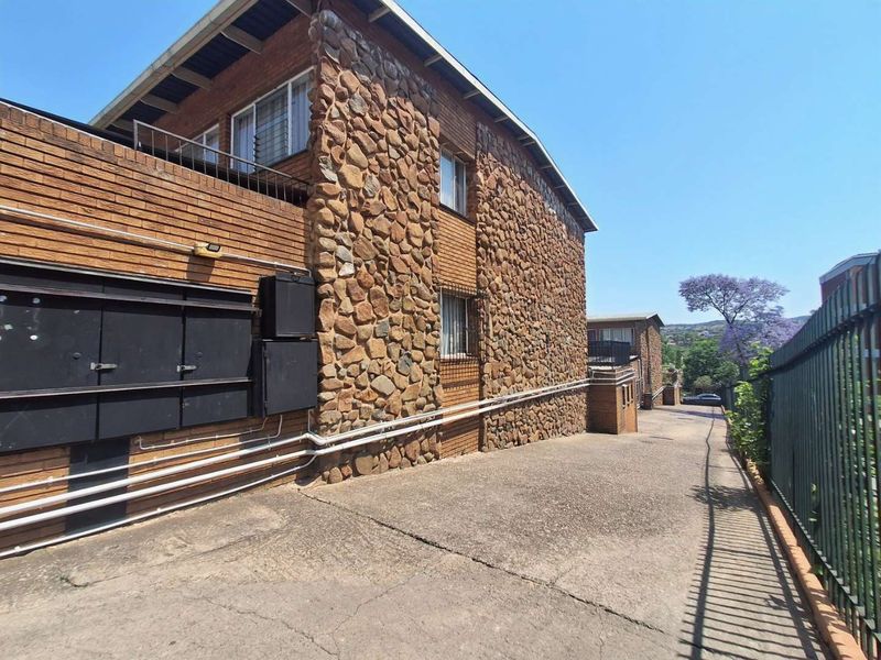 Exterior view of a townhouse complex featuring stone and brick facade, concrete driveway, and metal security fencing.
